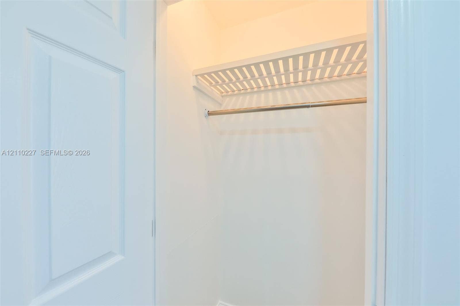 450 Bayshore Drive, Cape Coral, FL 33904 Interior closet featuring a white paneled door, built-in slatted shelving, and a metal hanging rod