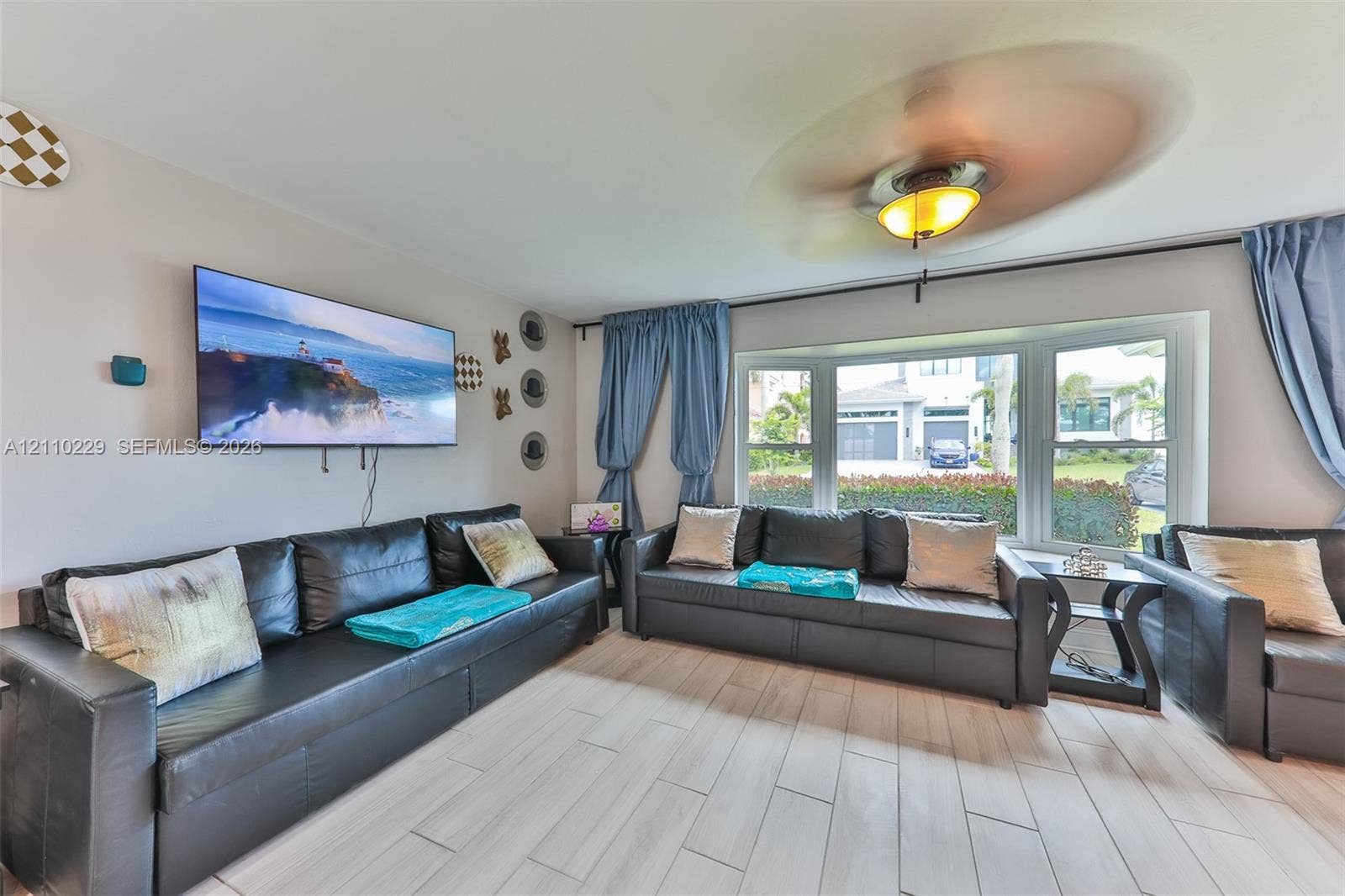 Large bay window featuring multi-pane glass, wood-finish tile flooring, and a ceiling-mounted light fixture with fan