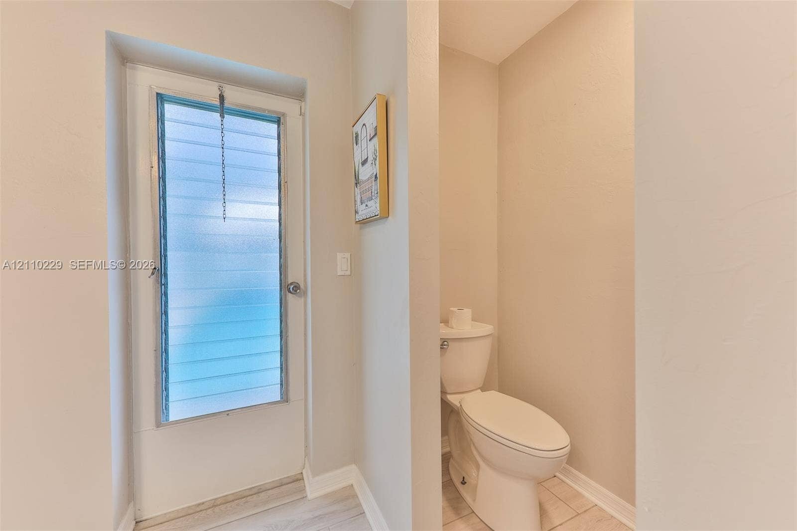 Full-height exterior door with frosted horizontal jalousie glass and an elongated white toilet