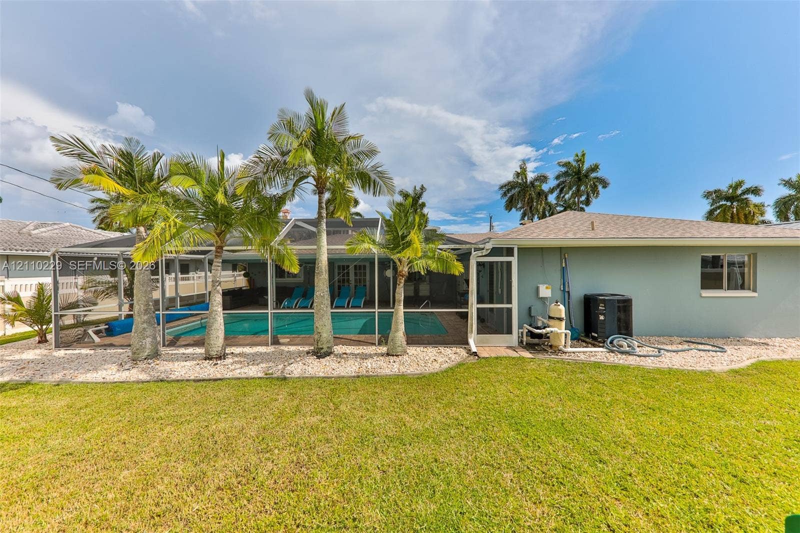 Screen-enclosed swimming pool featuring a concrete deck, manicured lawn, and mature palm trees