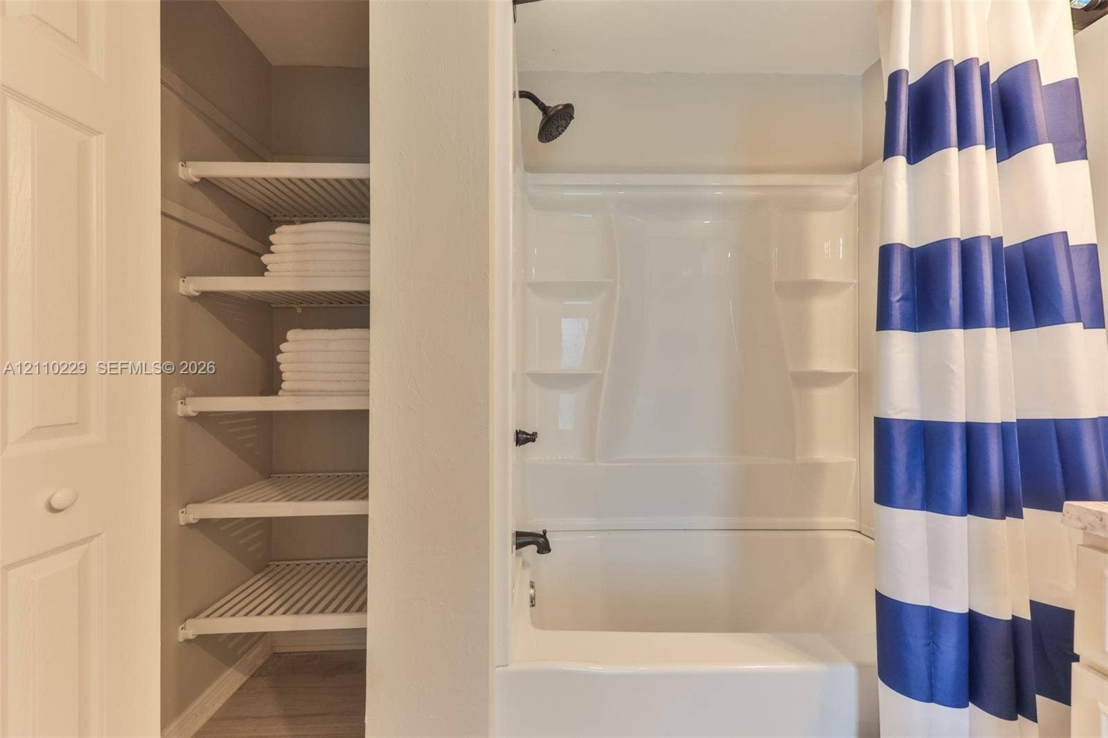 Bathroom featuring an integrated tub and shower surround with molded shelving, dark-finish hardware, and built-in wall shelving