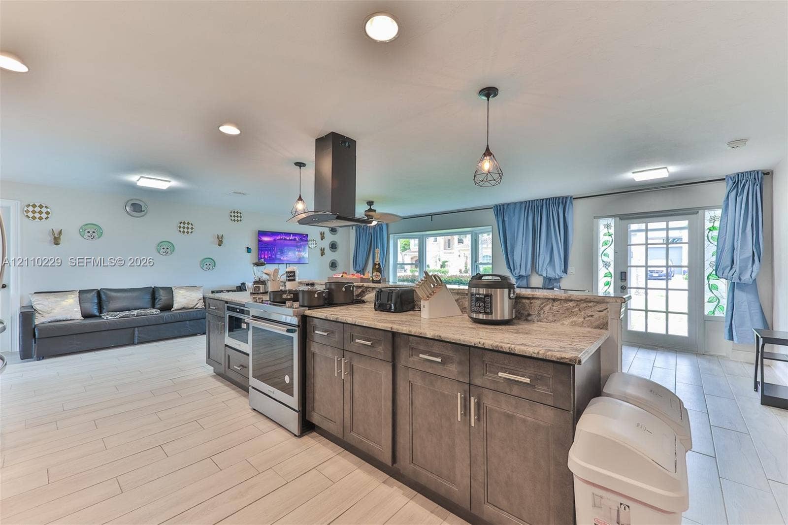 Kitchen featuring a stone-surface island, dark-toned cabinetry, stainless steel appliances, a modern chimney-style range hood, and tile flooring