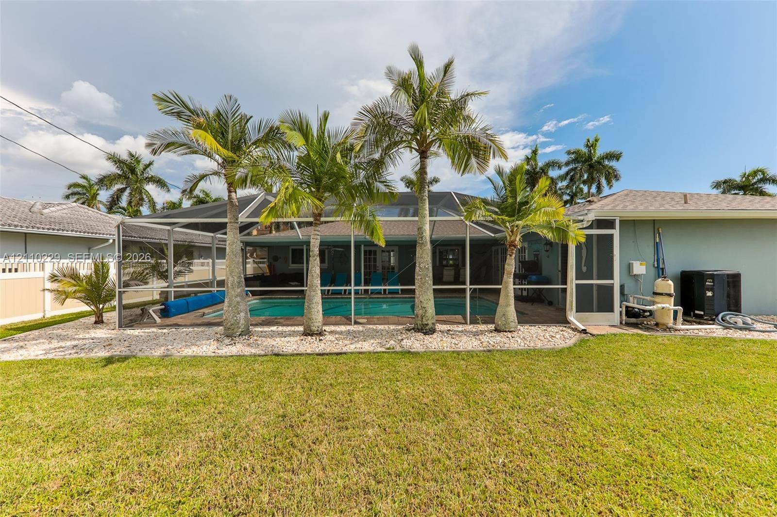 Screened-in pool area featuring a paved deck, mature palm trees, and a vinyl fence-enclosed backyard