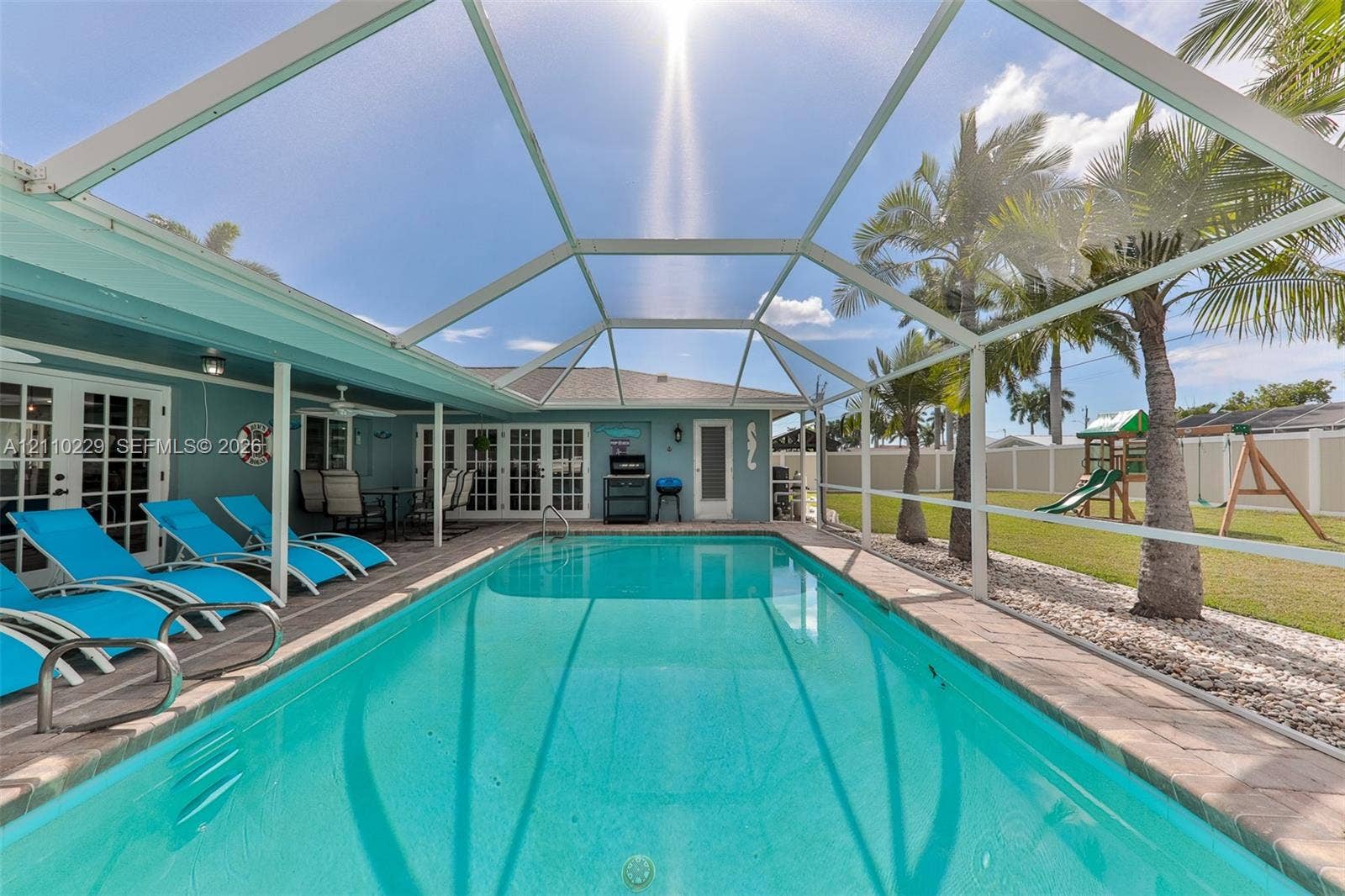 Screened pool enclosure featuring a concrete deck, stone-paver pool coping, and fenced backyard with palm trees