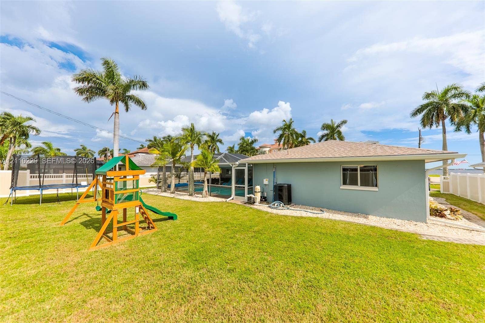 Spacious backyard featuring a manicured lawn, established palm trees, a screened-in swimming pool, and solid vinyl perimeter fencing