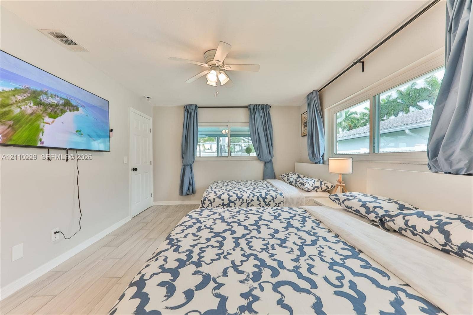 Neutral-toned interior space featuring light-toned wood-finish flooring, a multi-blade ceiling fan with integrated lighting, and multiple horizontal windows