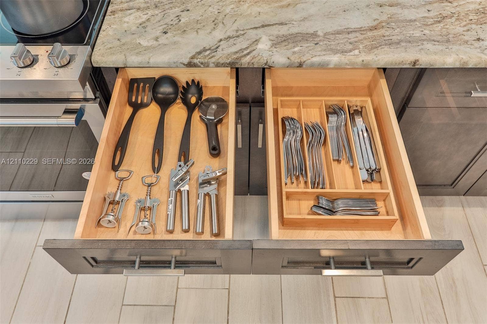 Custom cabinetry with integrated organizational drawer inserts, natural stone countertop, stainless steel range, and tile flooring