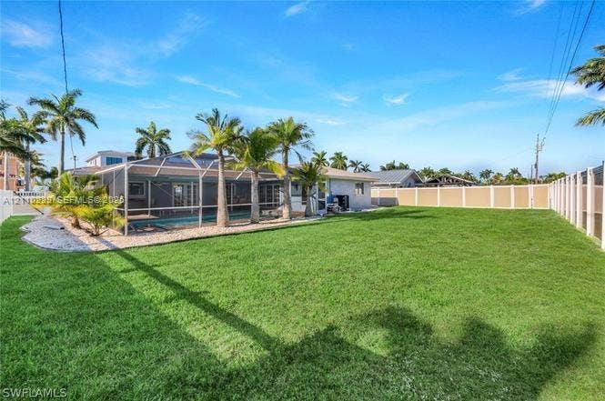 Expansive backyard featuring a manicured lawn, full-height privacy fencing, a screen-enclosed pool, and integrated landscape palms