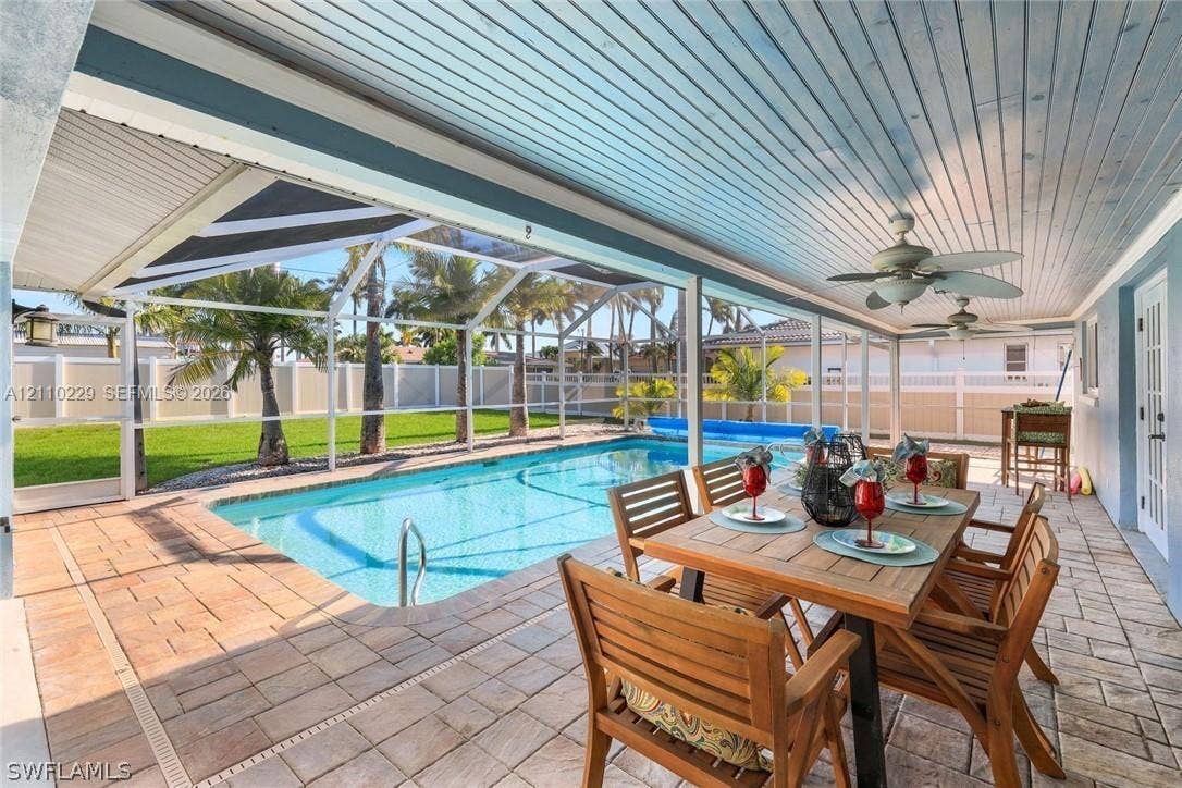 Covered lanai featuring a painted wood-plank ceiling with dual ceiling fans, paver patio, screened enclosure, and an in-ground swimming pool