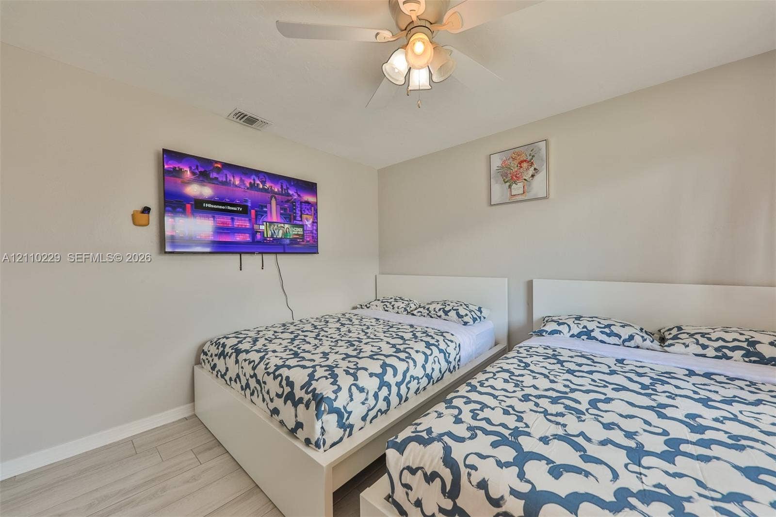 Neutral-toned interior featuring wood-finish flooring, a ceiling fan with integrated lighting, and a wall-mounted display