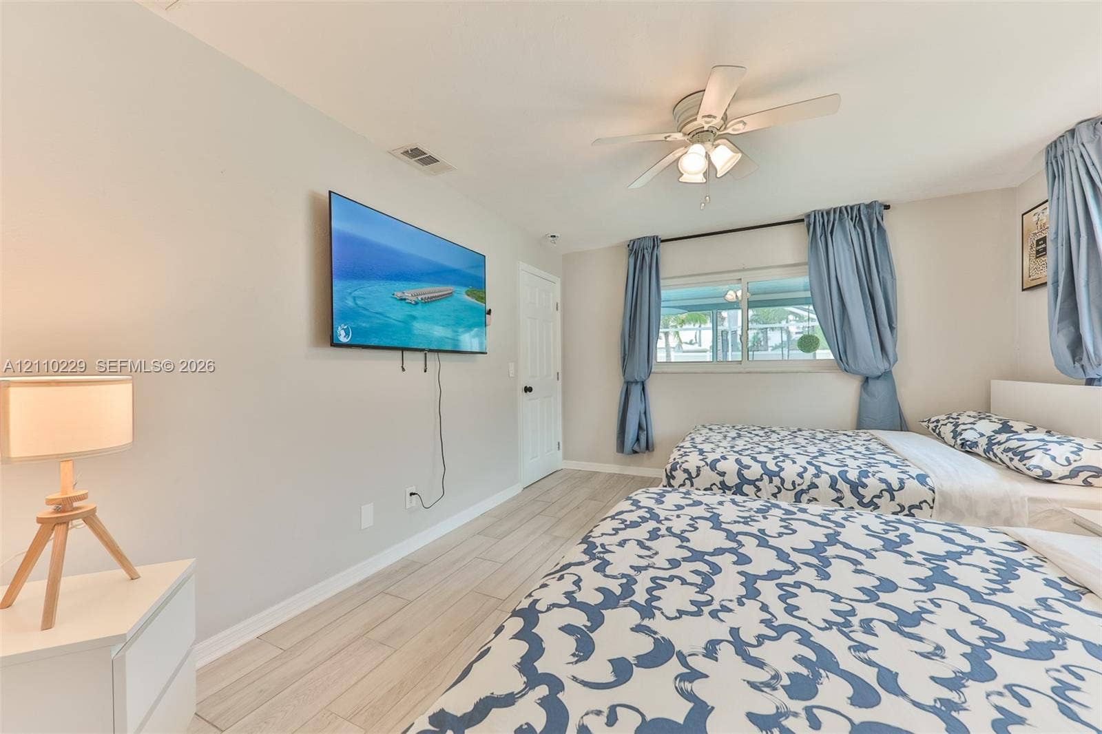 Neutral-toned walls, wood-finish flooring, ceiling fan with integrated lighting, and dual windows
