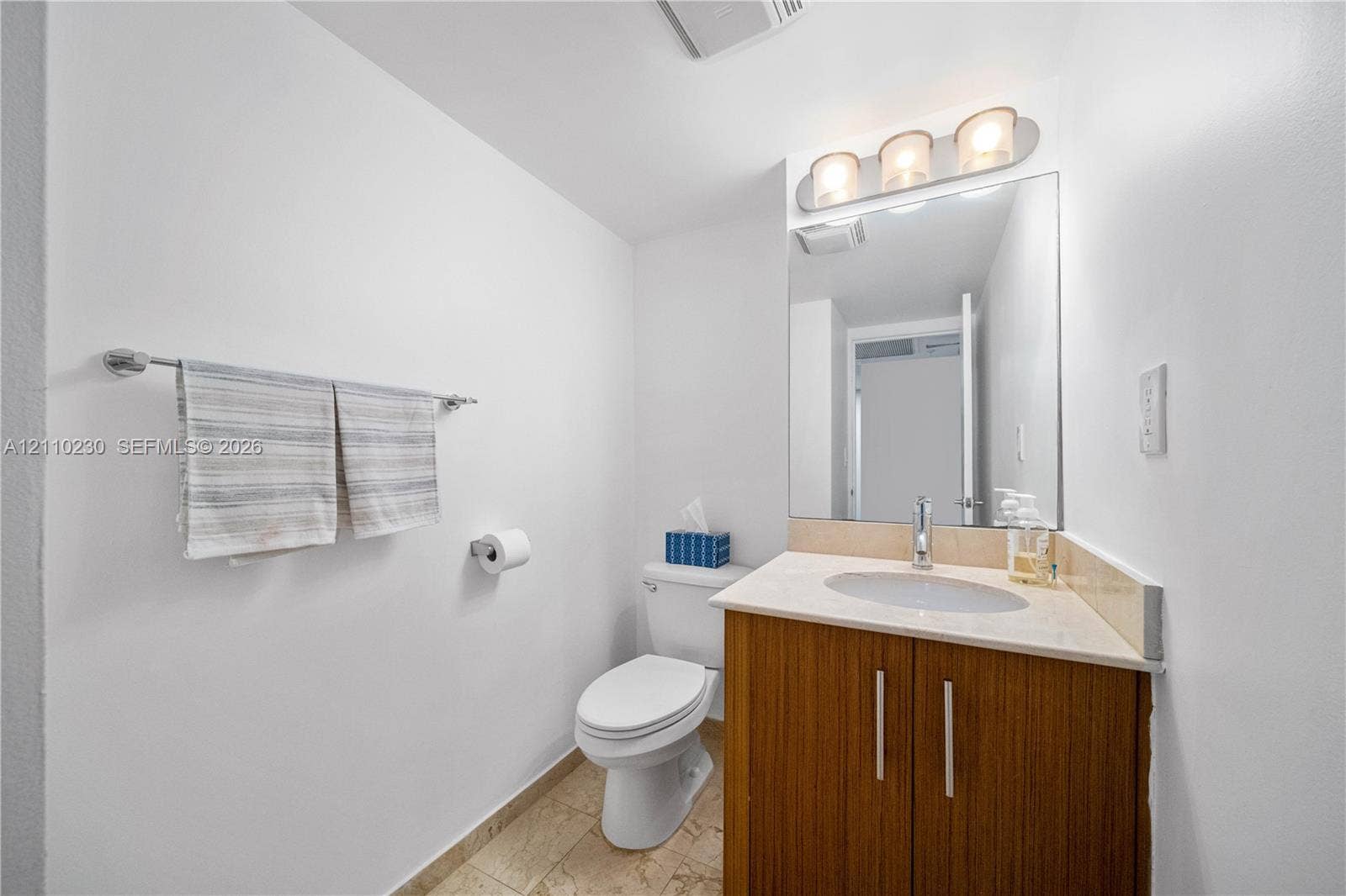 Bathroom featuring a wood-finish vanity with a stone-surface countertop, an oval undermount sink, a polished metal faucet, a large frameless mirror, and a three-light fixture