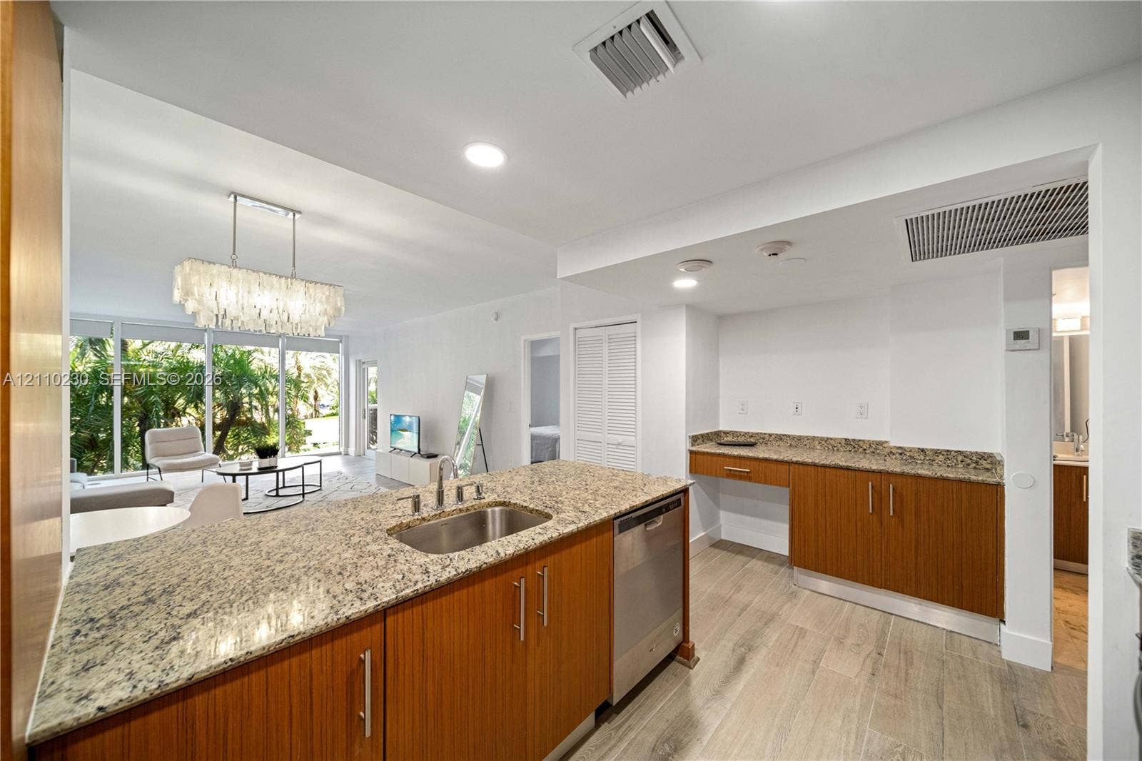 Kitchen featuring stone countertops, wood-finish cabinetry, a stainless steel undermount sink, built-in dishwasher, and wood-finish flooring