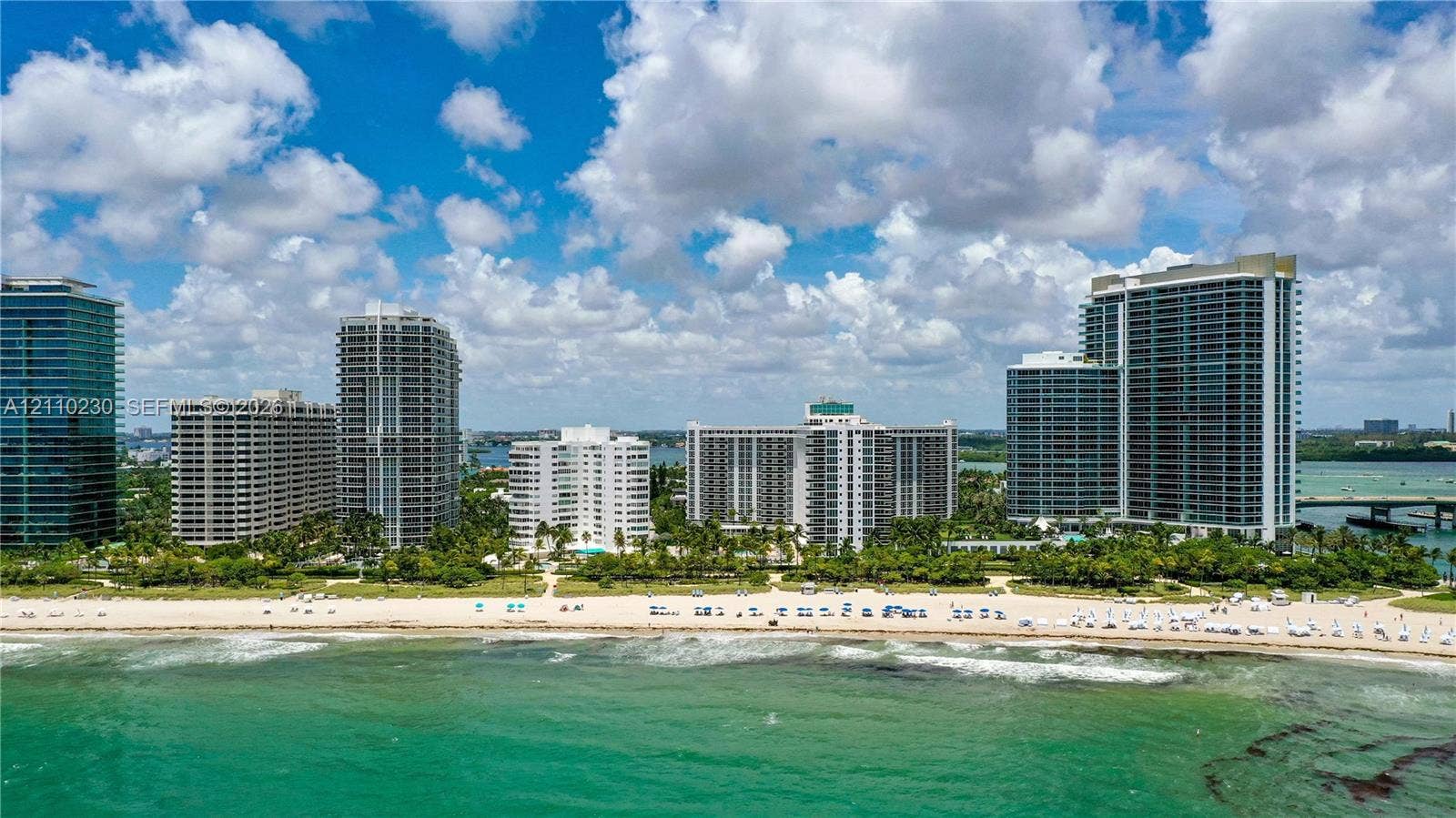 Aerial perspective of coastal high-rise structures featuring direct shoreline access, sandy beachfront, and perimeter landscaping