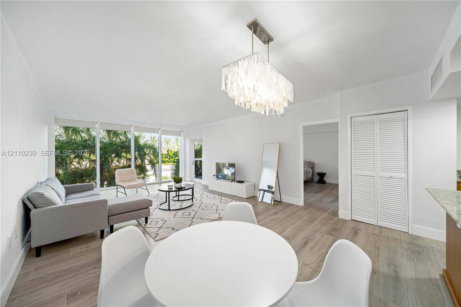 Open-concept room featuring floor-to-ceiling windows, wood-finish flooring, a tiered crystal chandelier, and louvered closet doors