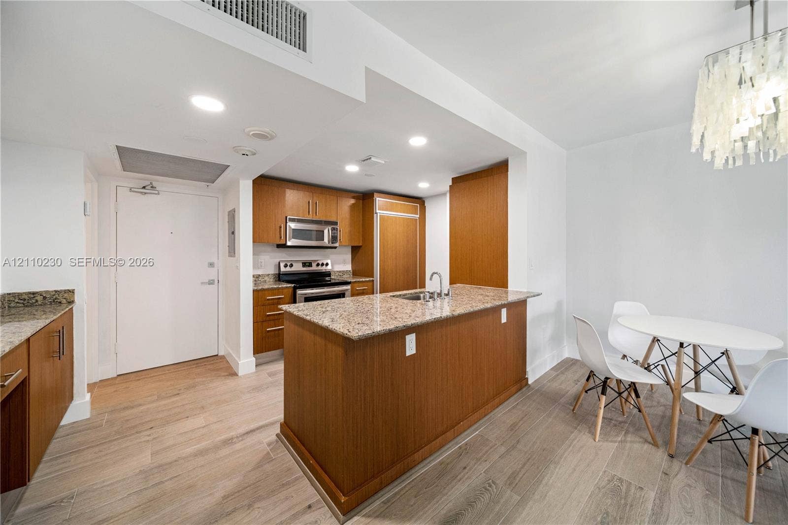 Kitchen featuring wood cabinetry, stone countertops, a center island with a built-in sink, stainless steel appliances, and wood-finish flooring