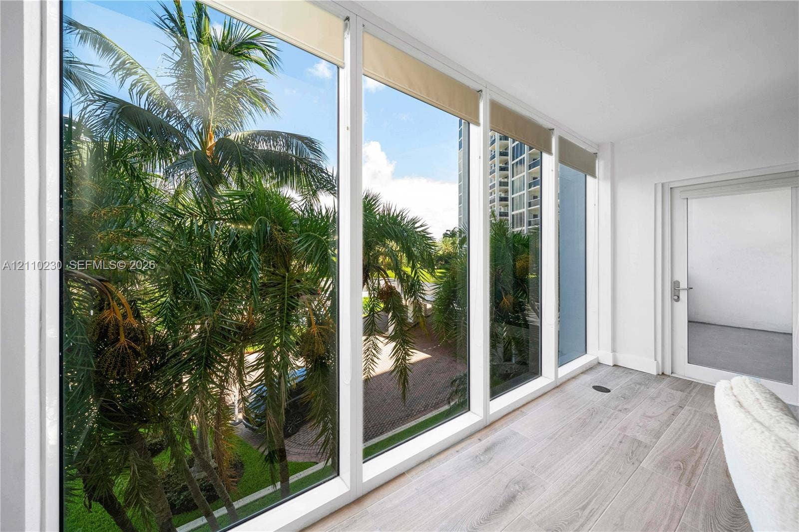 Floor-to-ceiling windows, wood-finish flooring, and single-panel glass door with metallic hardware
