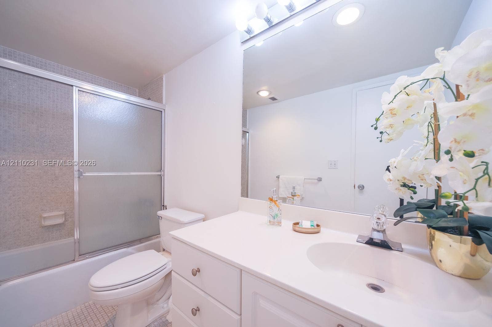 19370 Collins Avenue, #622, Sunny Isles Beach, FL 33160 Bathroom featuring white vanity cabinetry, integrated countertop with a molded sink, polished chrome faucet, full-width mirror, and a shower-tub combination with a sliding glass door