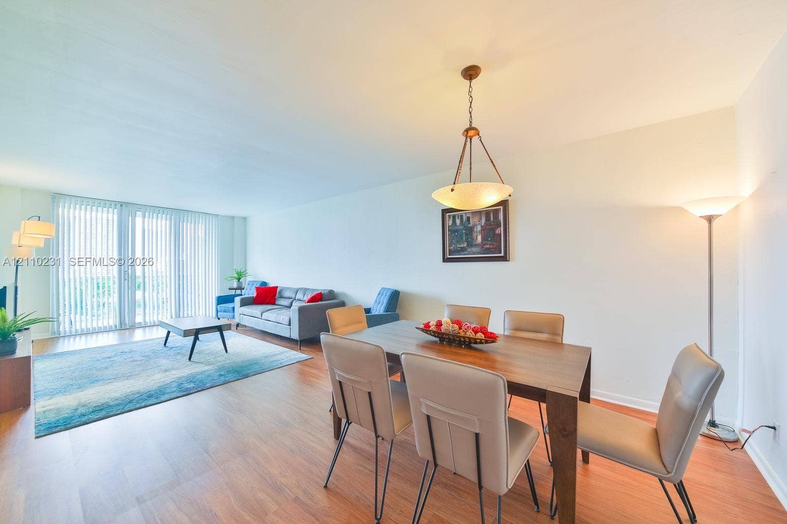 19370 Collins Avenue, #622, Sunny Isles Beach, FL 33160 Open-concept area featuring wood-finish flooring, a suspended metal-frame pendant light fixture, and floor-to-ceiling sliding glass doors with vertical blinds