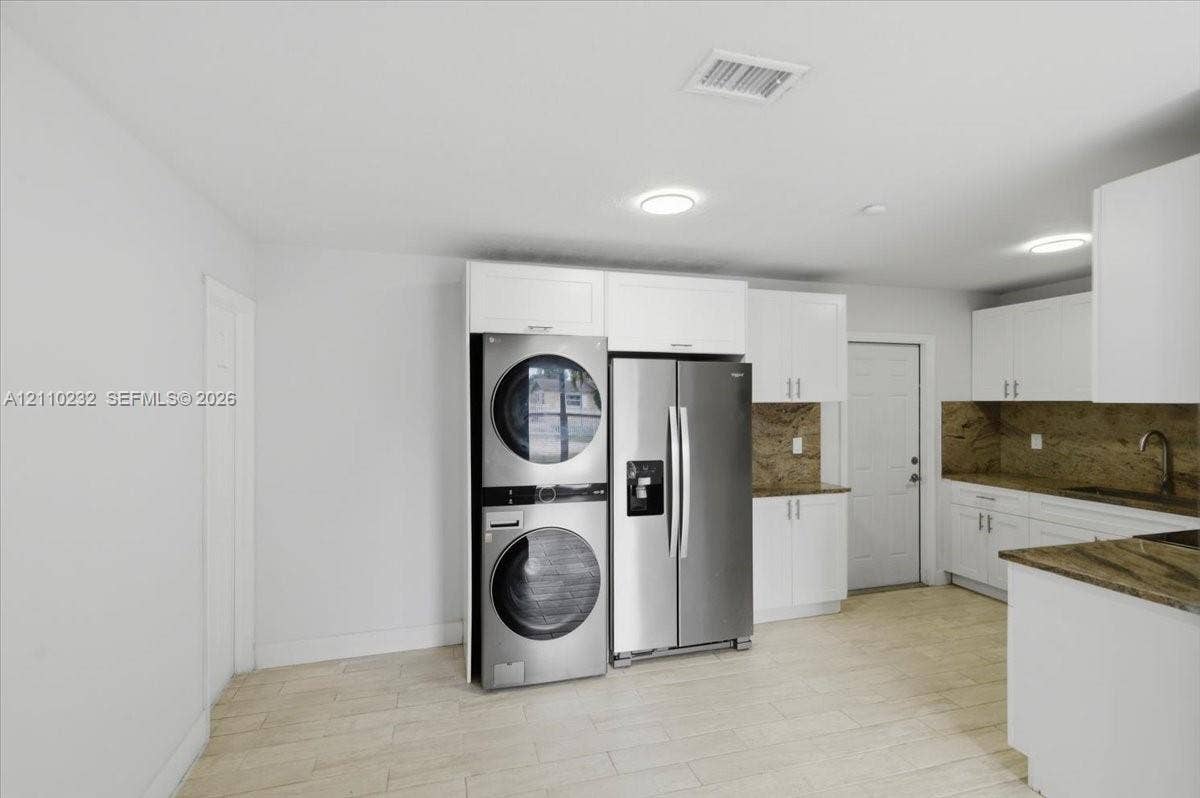 White cabinetry featuring shaker-style doors, stone-finish countertops, stainless steel appliances, and wood-finish flooring