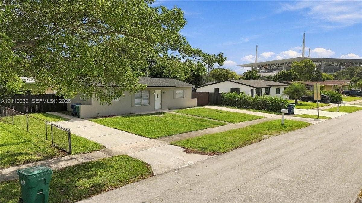 Single-story exterior featuring a concrete driveway, metal chain-link fencing, and a grass lawn