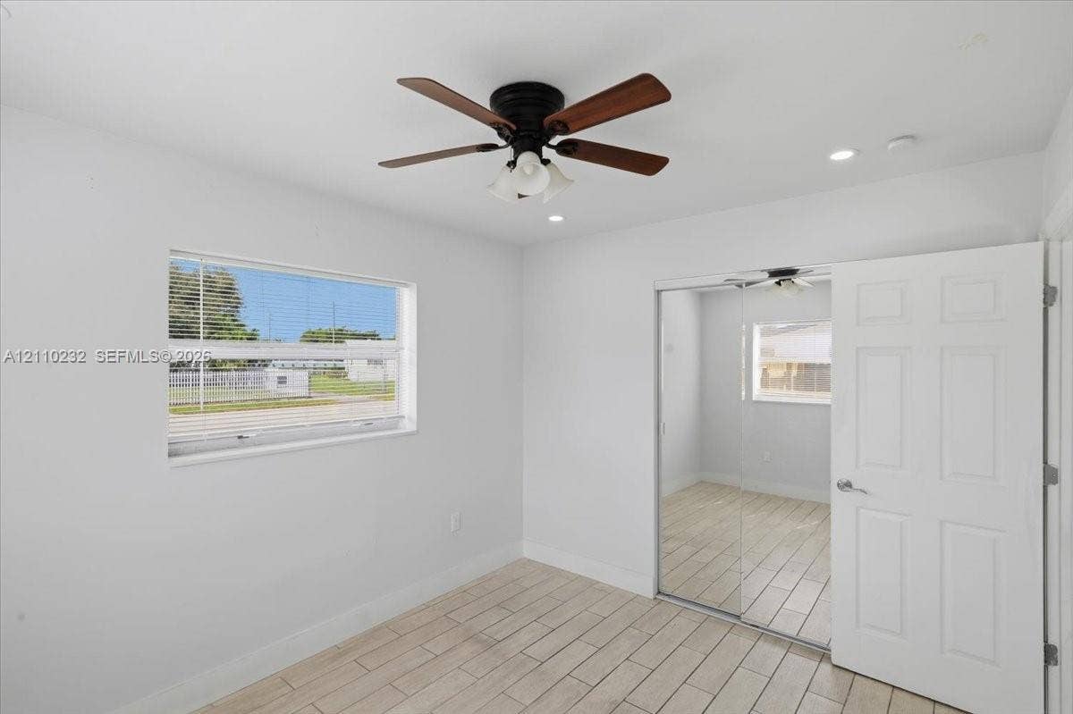 Room featuring wood-finish tile flooring, a multi-blade ceiling fan with integrated lighting, recessed lighting, and a closet with sliding mirrored doors