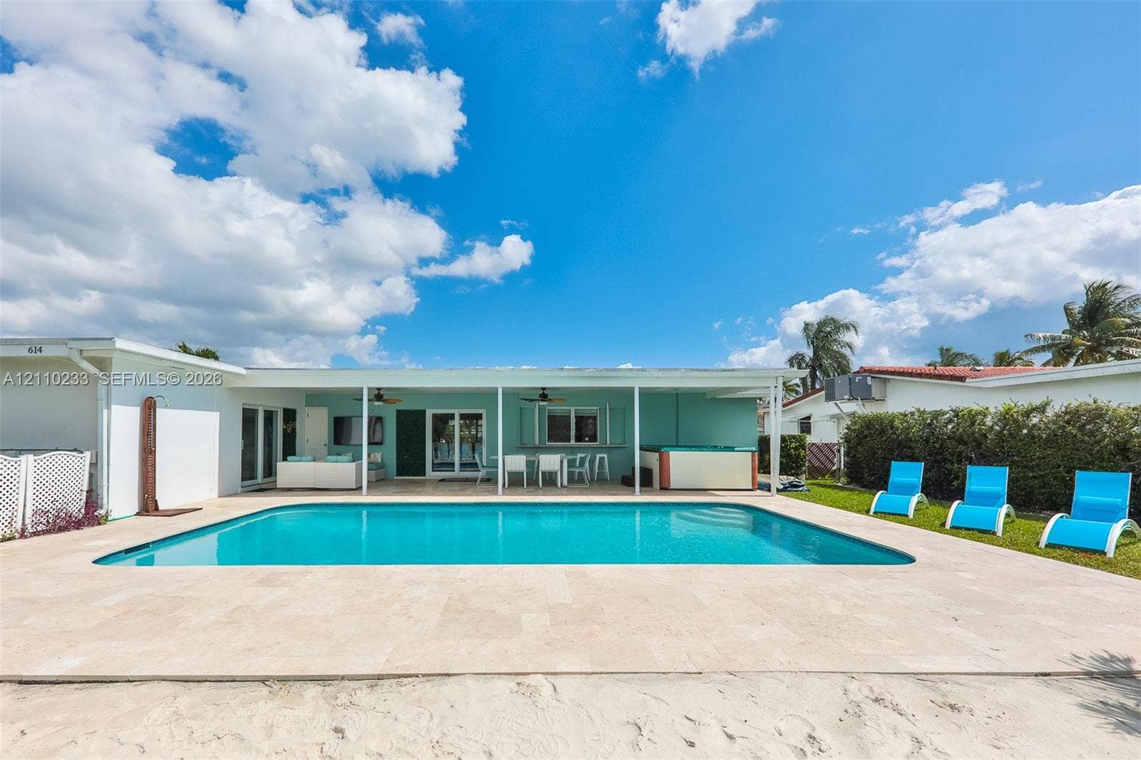 614 S Crescent Drive, Hollywood, FL 33021 Rectangular in-ground swimming pool featuring a light-toned stone pool deck, covered outdoor patio, built-in hot tub, and exterior ceiling fans