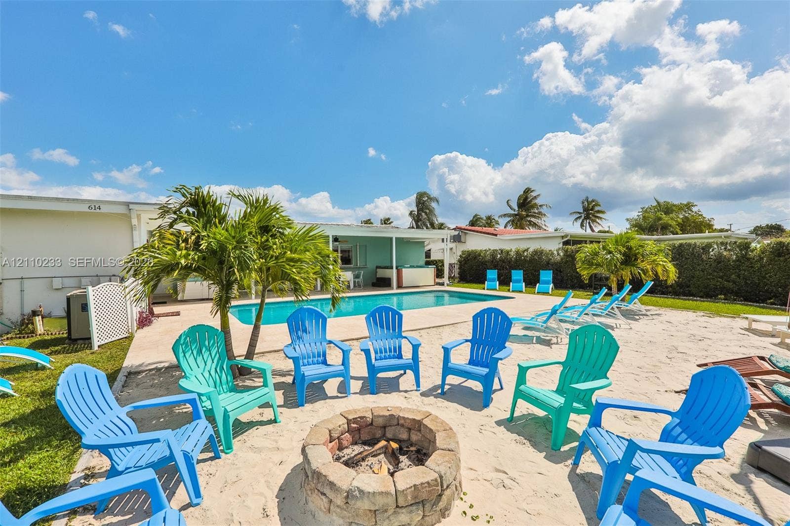 614 S Crescent Drive, Hollywood, FL 33021 Rectangular swimming pool with a concrete surround, circular stone-block fire pit, and mature palm trees