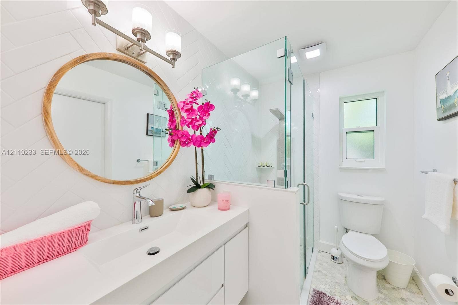 614 S Crescent Drive, Hollywood, FL 33021 Bathroom featuring a wall-mounted vanity with integrated sink, glass-enclosed shower, round mirror with wood frame, three-light vanity fixture, and herringbone-patterned tile wall