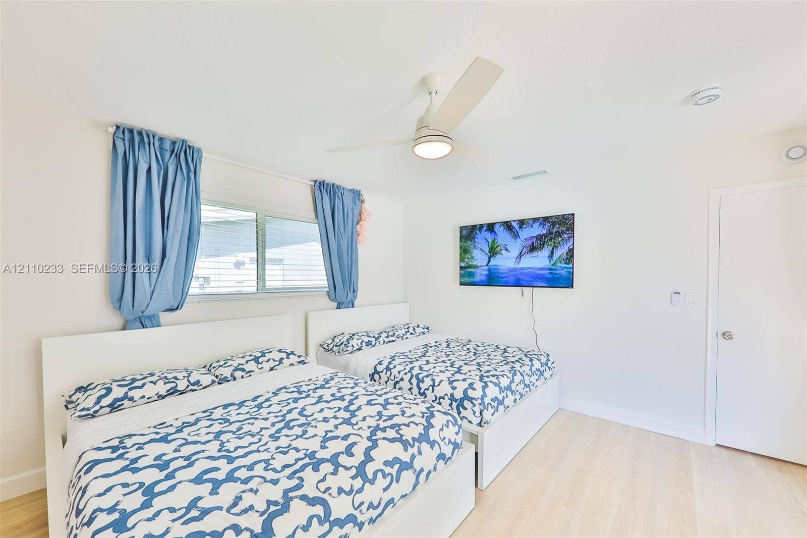 614 S Crescent Drive, Hollywood, FL 33021 Neutral-toned room featuring wood-finish flooring, a white three-blade ceiling fan with integrated lighting, and a horizontal sliding window