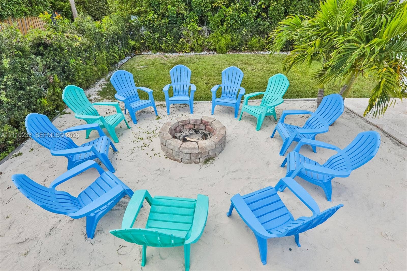 614 S Crescent Drive, Hollywood, FL 33021 Backyard featuring a circular stone fire pit, sand ground cover, manicured lawn, and perimeter hedging