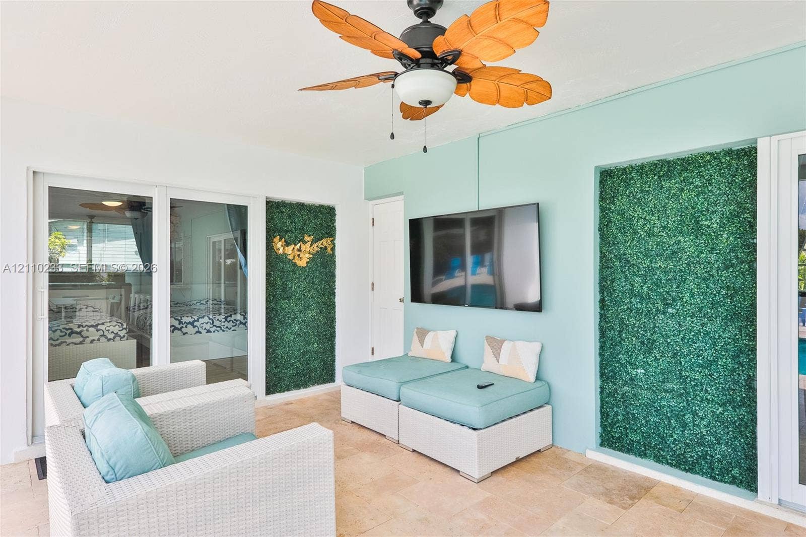 614 S Crescent Drive, Hollywood, FL 33021 Covered outdoor living space featuring stone flooring, a ceiling fan with leaf-style blades, and decorative faux-greenery wall panels