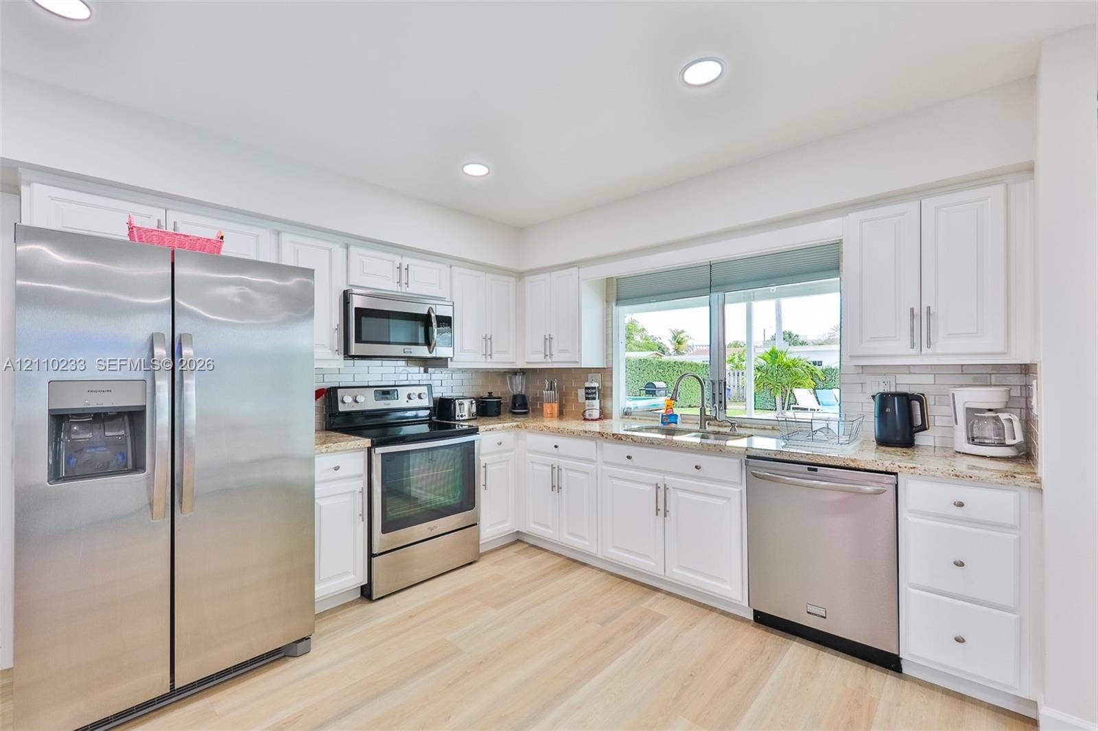 614 S Crescent Drive, Hollywood, FL 33021 Kitchen featuring white shaker-style cabinetry, light-toned stone countertops, subway tile backsplash, wood-finish flooring, and stainless steel appliances