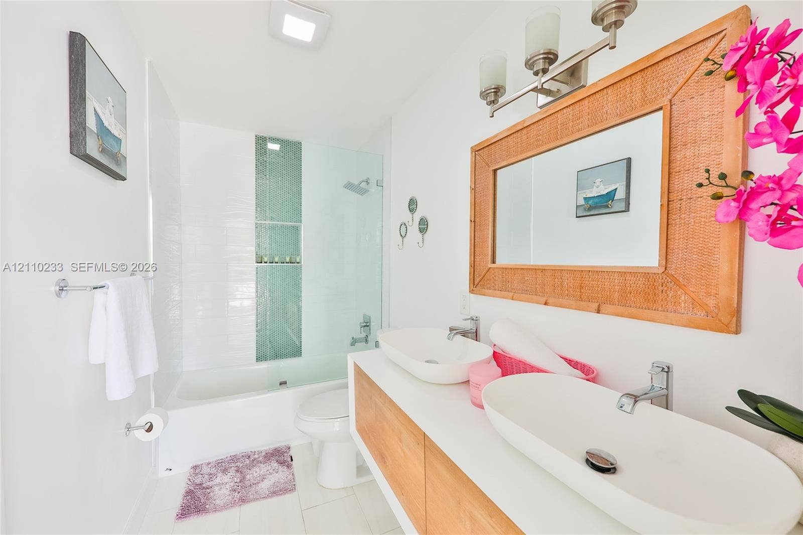 614 S Crescent Drive, Hollywood, FL 33021 Floating double vanity featuring light wood-finish cabinetry, rectangular vessel sinks, and polished chrome hardware, complemented by a glass-enclosed shower with a vertical mosaic tile accent