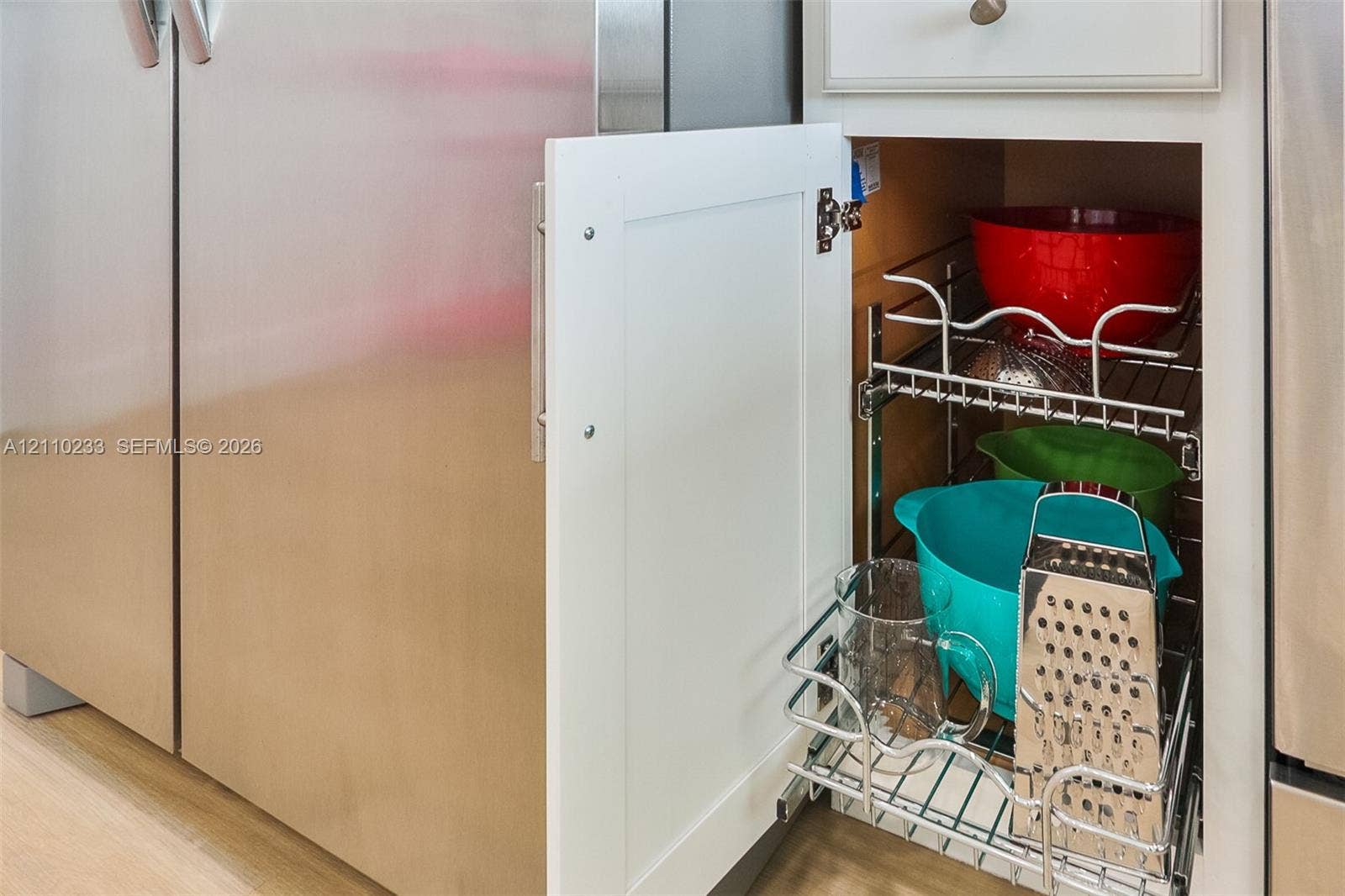 614 S Crescent Drive, Hollywood, FL 33021 Custom white shaker-style cabinetry featuring an integrated pull-out chrome wire storage rack, set beside a stainless steel refrigerator