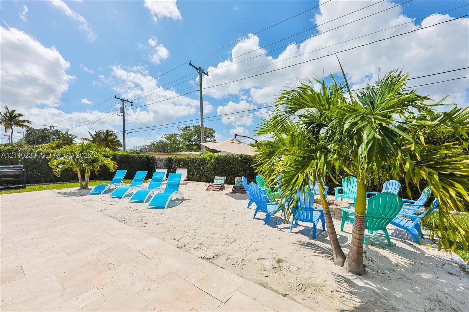 614 S Crescent Drive, Hollywood, FL 33021 Outdoor living area featuring a light-toned stone paved patio, integrated sand-filled recreational space, and mature palm trees