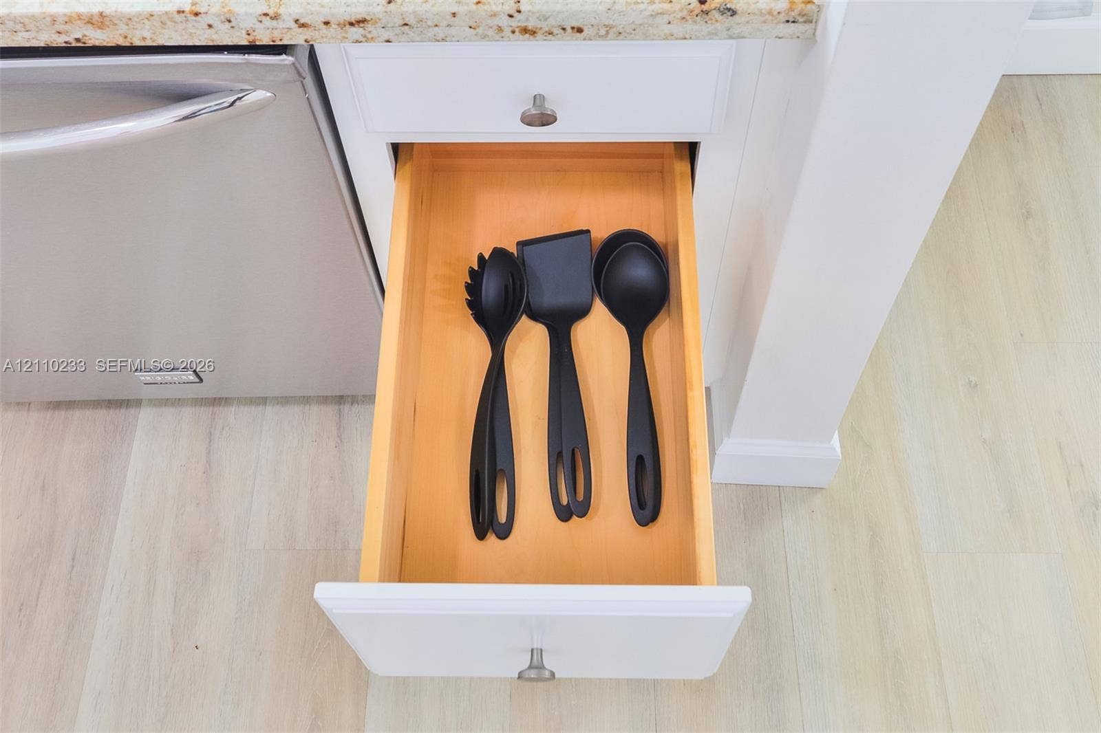 614 S Crescent Drive, Hollywood, FL 33021 Custom-fit cabinetry featuring a pull-out drawer with a natural wood interior, white shaker-style paneling, a stainless steel dishwasher, and stone-surfaced countertops