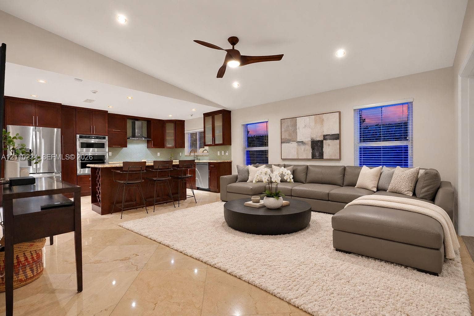 Open-concept interior featuring vaulted ceilings, polished tile flooring, recessed lighting, and a kitchen equipped with dark wood-finish cabinetry, a central island with bar seating, and stainless steel built-in appliances