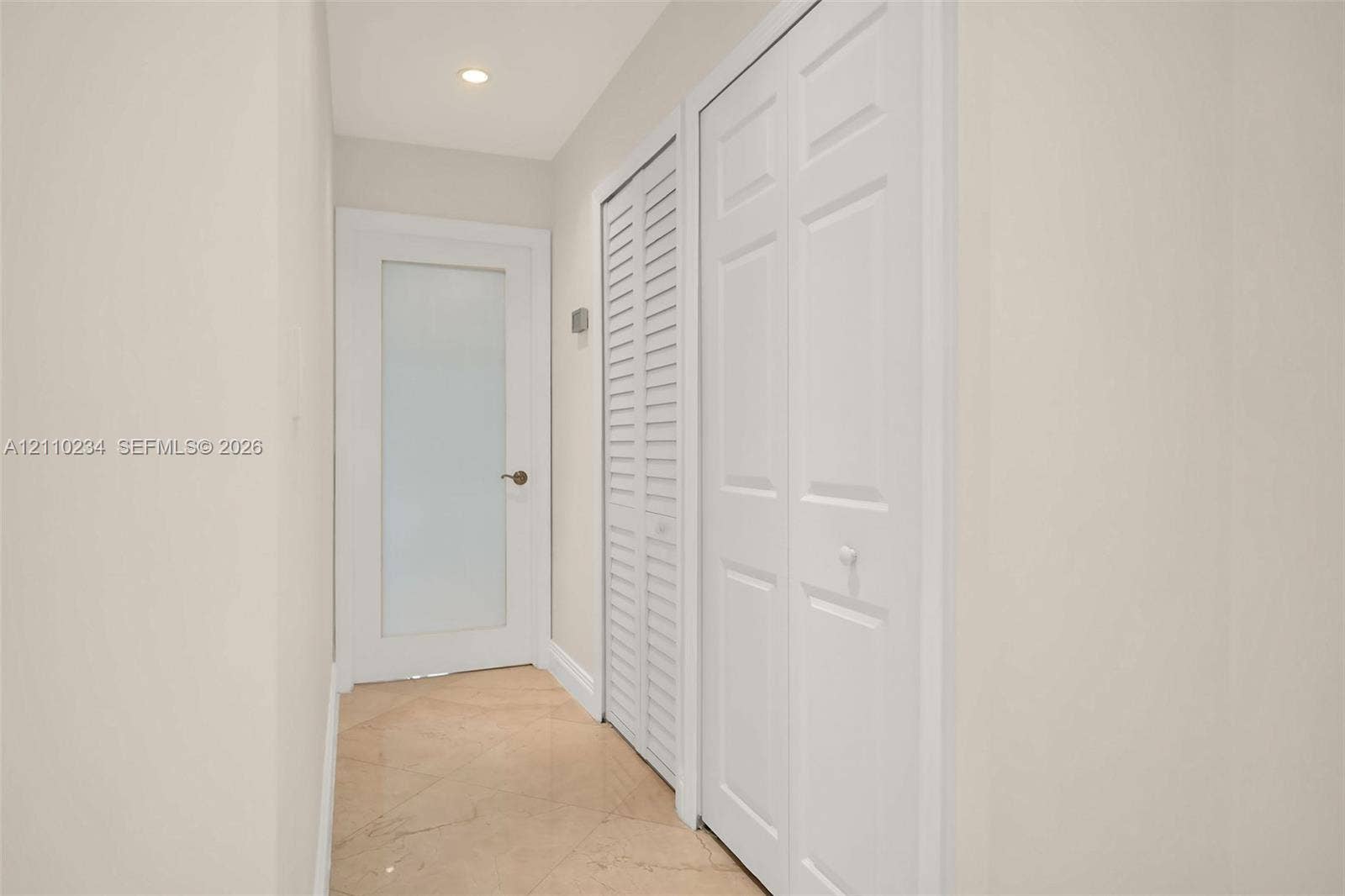Neutral-toned interior space featuring stone flooring, a door with a frosted glass panel, and dual built-in closets with white louvered and paneled doors