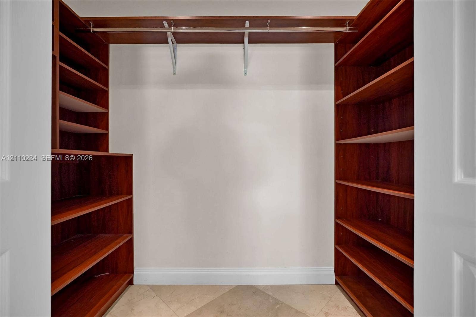 Walk-in closet featuring custom wood-finish shelving units, integrated hanging rods, and tile flooring