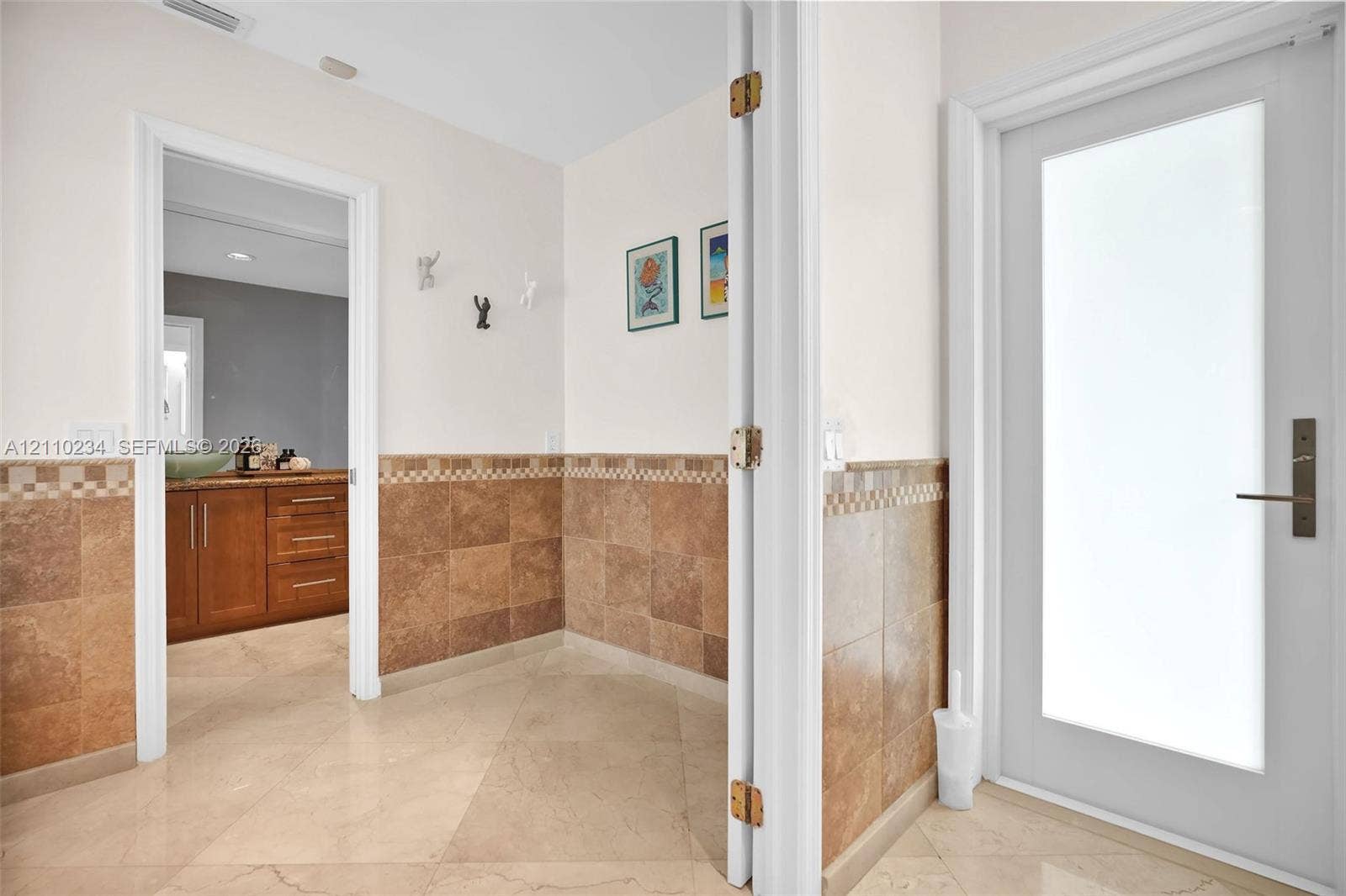 Entry area featuring large-format diagonal tile flooring, wall-mounted hardware, and wainscoting with decorative tile accents