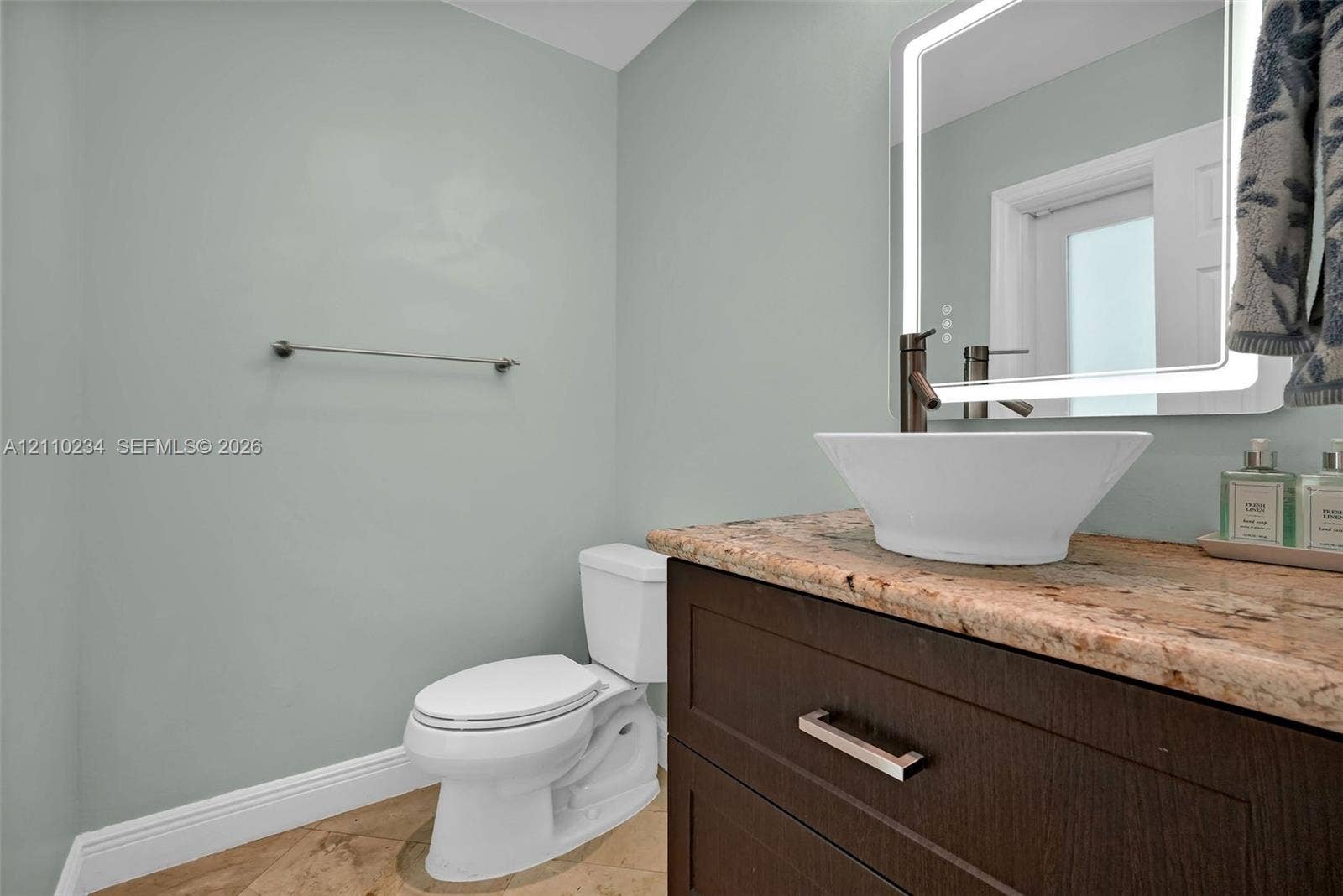 Dark wood vanity featuring a stone countertop, white vessel sink, brushed metal faucet, and an integrated LED-backlit mirror