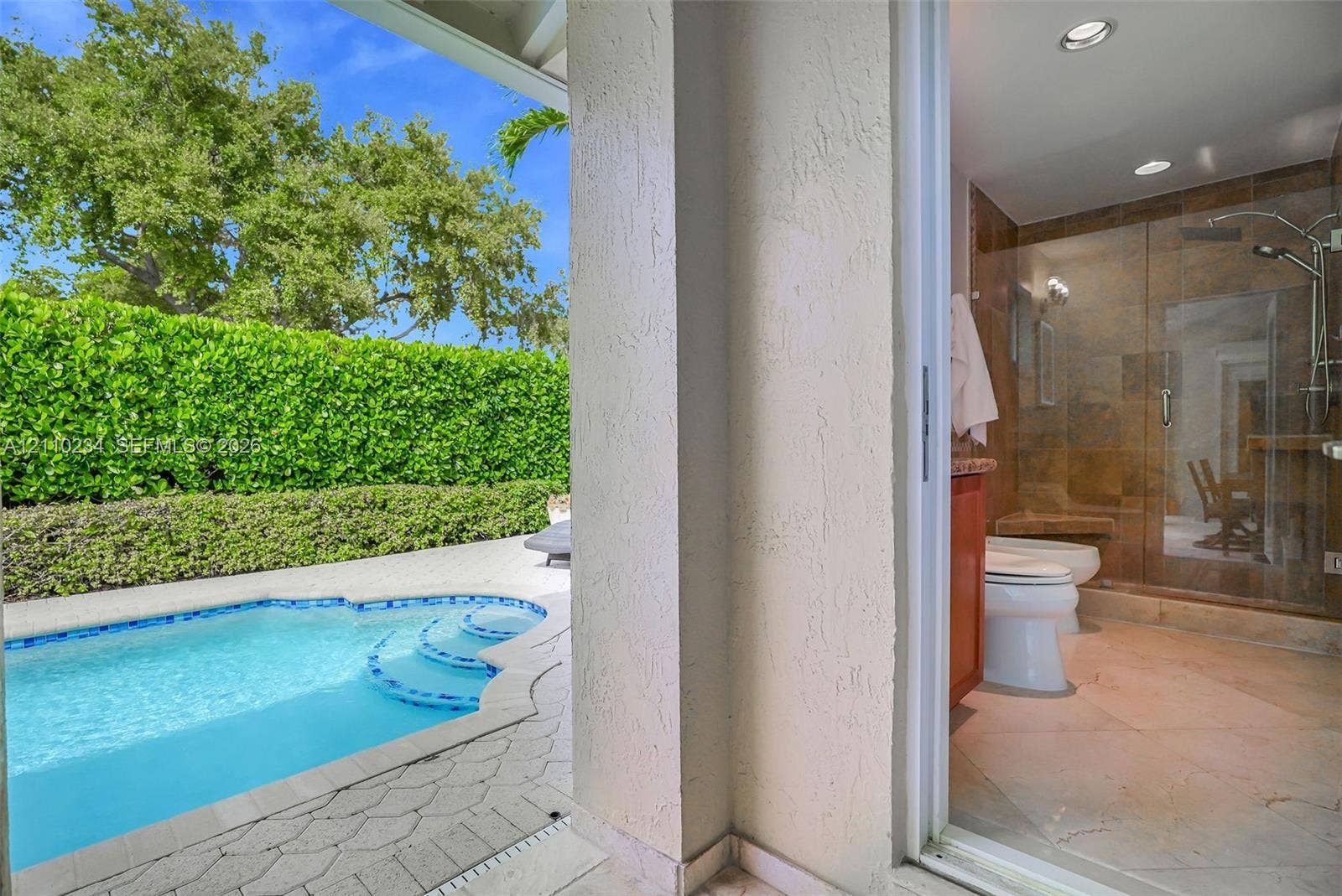 In-ground pool with stone paver surround, recessed shower lighting, glass-enclosed shower stall with tile wall, and stucco exterior walls