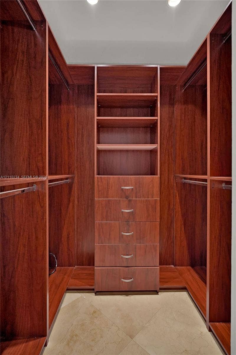 Custom walk-in closet featuring floor-to-ceiling wood-finish cabinetry, built-in shelving, a five-drawer dresser unit with metallic pulls, multiple integrated clothing rods, and tile flooring