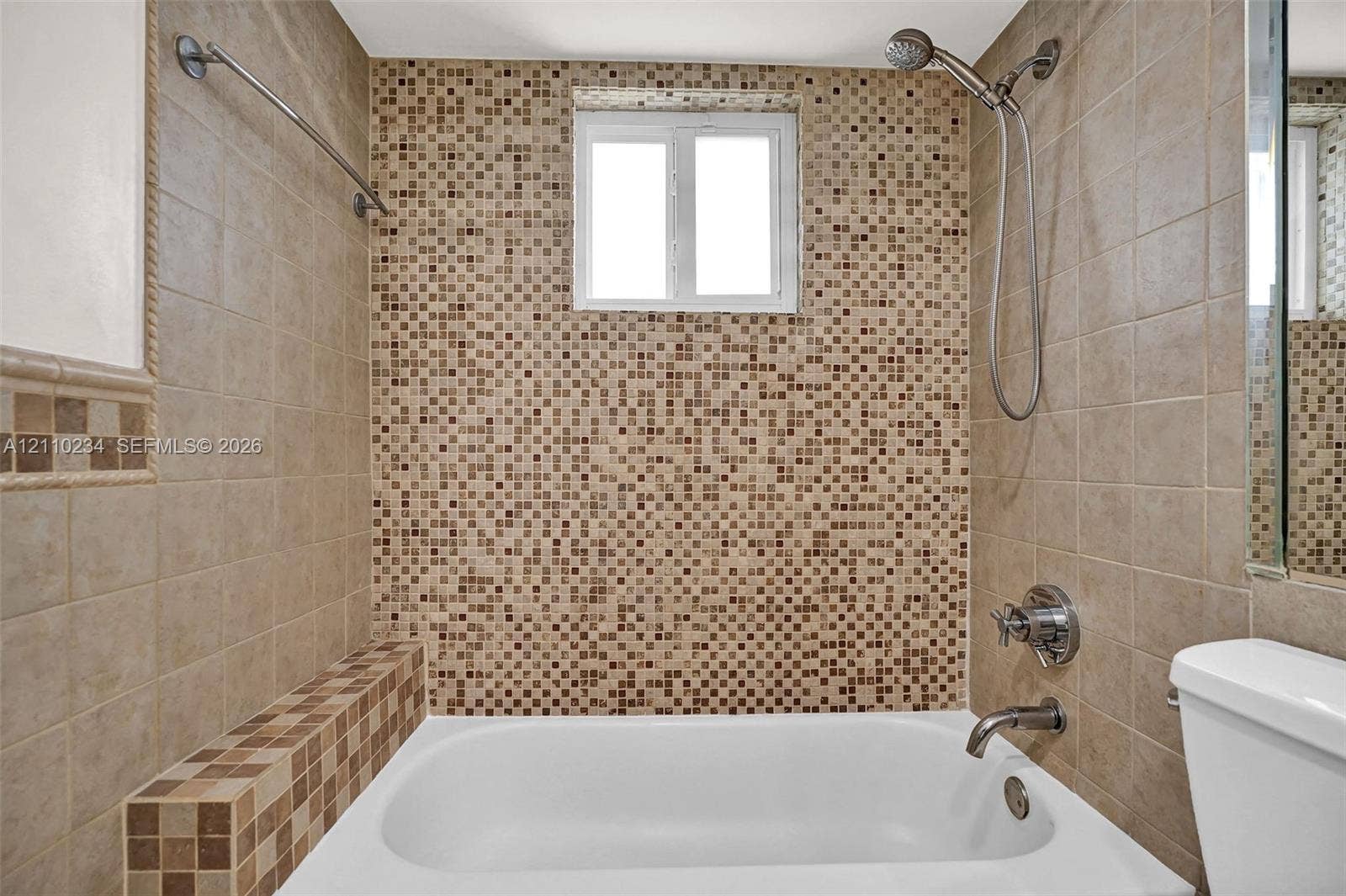 Bathroom featuring a porcelain soaking tub with metallic faucet fixtures, multi-textured square mosaic wall tiles, and a double-hung window