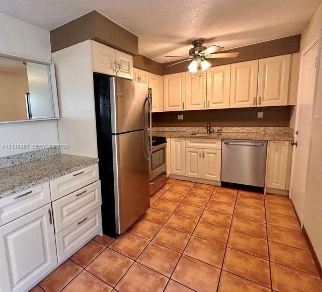 Kitchen featuring off-white cabinetry, speckled stone-finish countertops, stainless steel appliances, and ceramic tile flooring