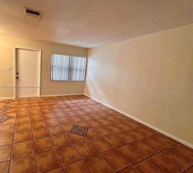 Interior space featuring oversized square ceramic floor tiles with decorative pattern insets, neutral-toned wall paint, and a window with vertical blinds