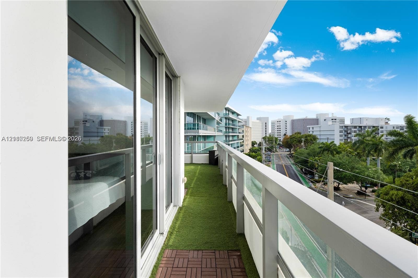 Covered balcony with a glass-paneled railing, synthetic turf flooring, and floor-to-ceiling sliding glass doors
