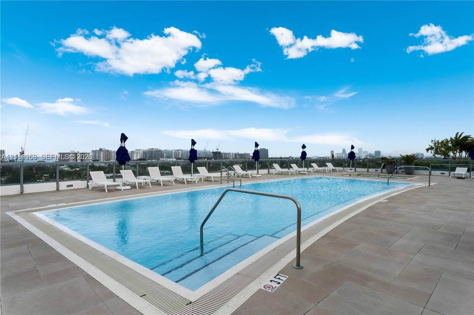 Rooftop swimming pool featuring a tiled deck, metal railing, and stainless steel ladder