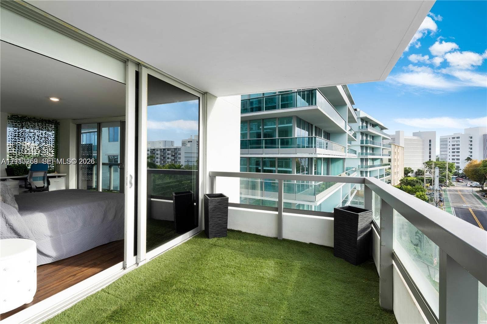 Covered balcony featuring synthetic turf flooring, floor-to-ceiling glass sliding doors, and a metal railing with glass panels